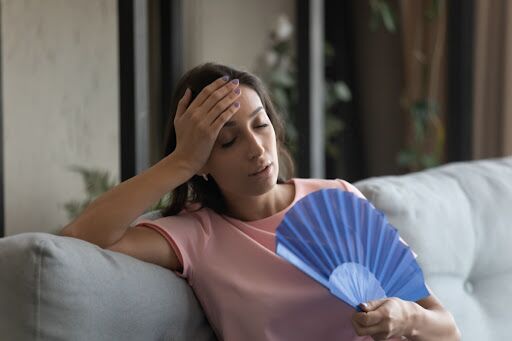 A woman sitting on the couch with a fan.