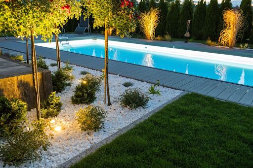 A backyard with a pool and landscape lighting.